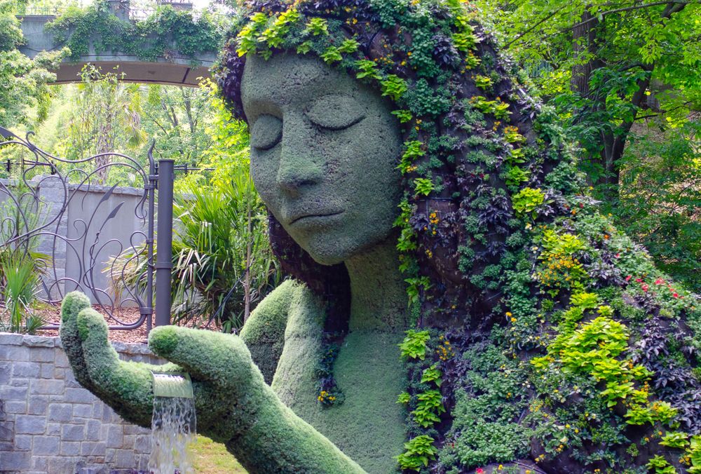 A large garden sculpture depicting a face covered in flowering vines and plants.