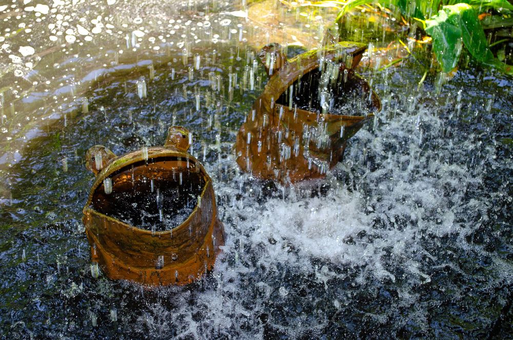 A wooden barrel fountain creating a dynamic water splash effect in sunlight.