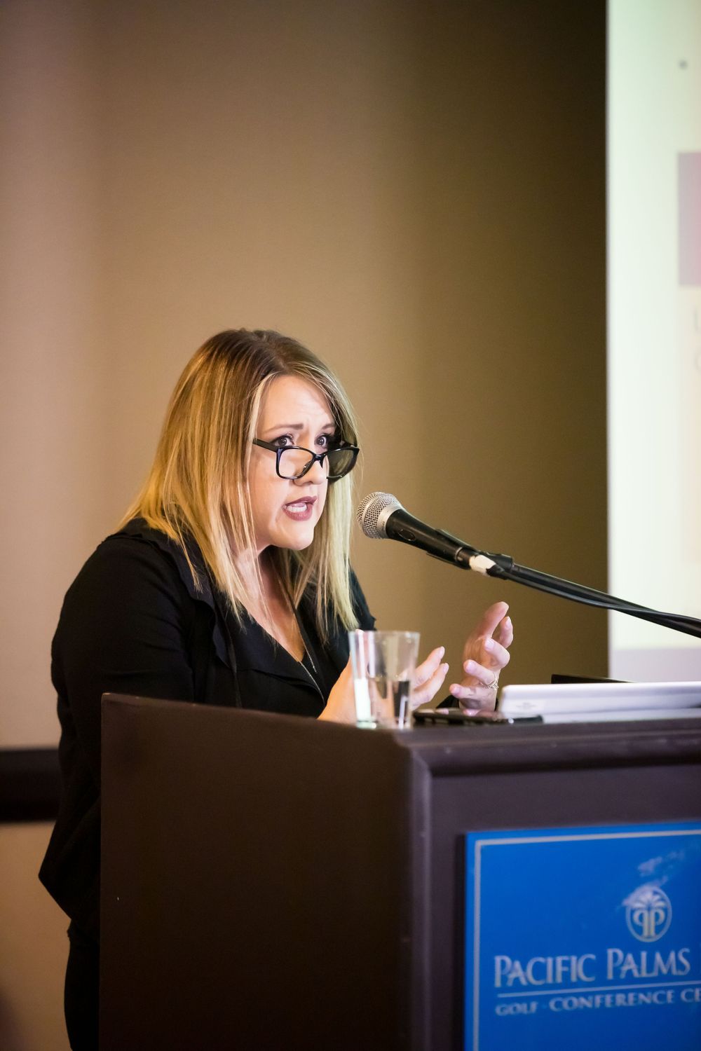 Professional speaker delivering a presentation from behind a podium at a conference venue.
