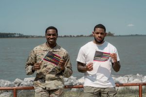 Military service member and civilian posing together by waterfront railing.