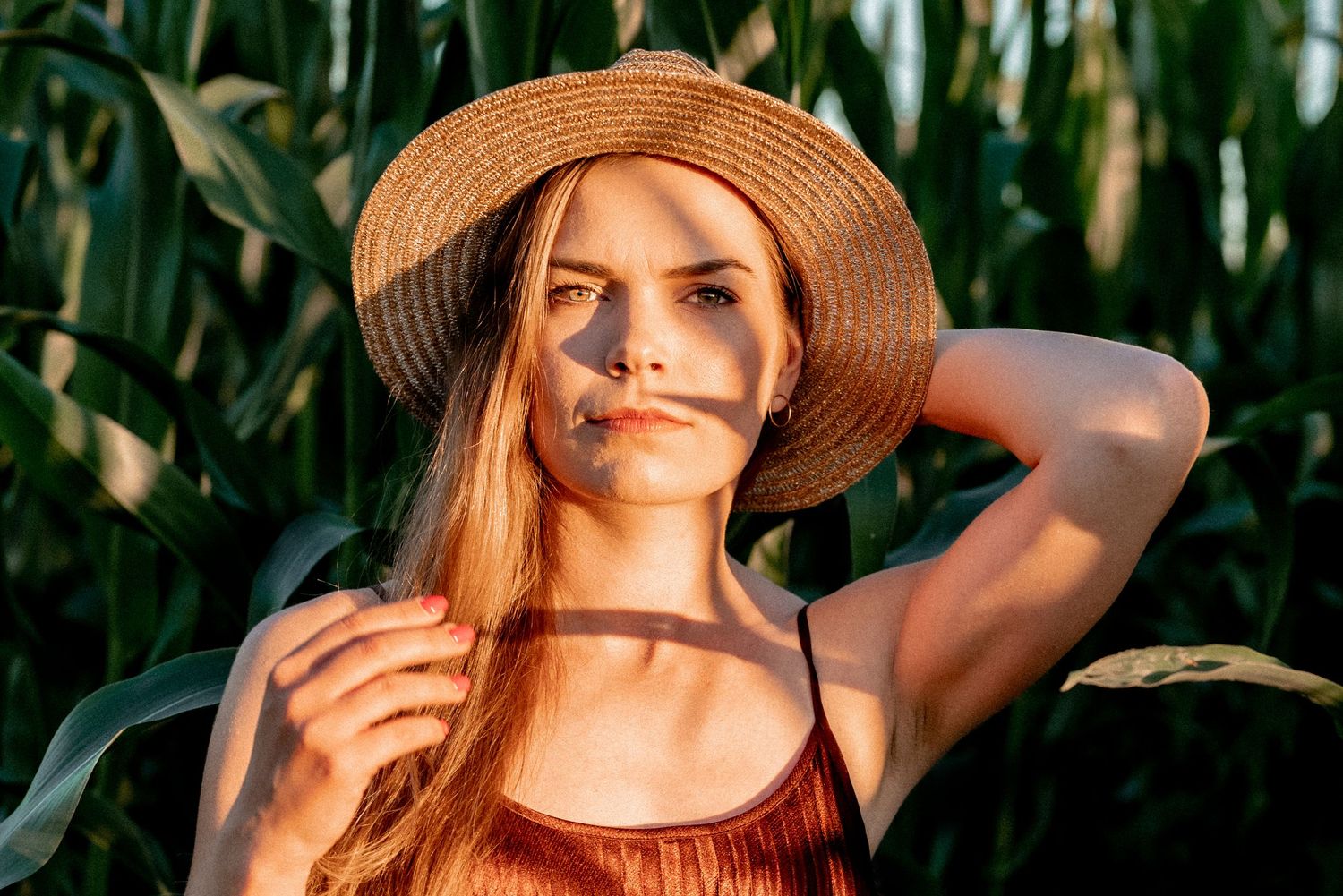 Summer portrait in straw hat amidst cornfield during golden hour.