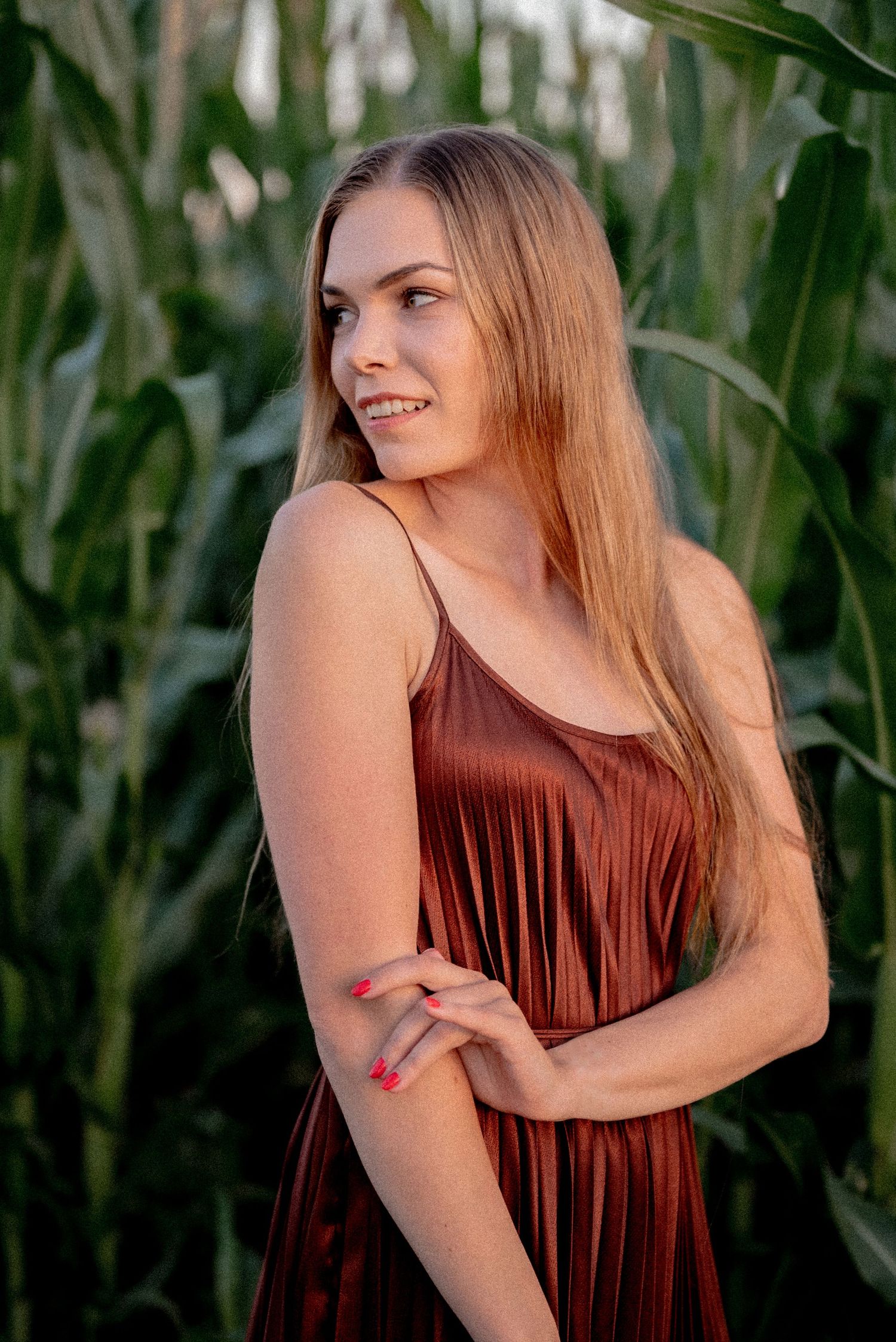 Natural summer portrait in rust-colored dress against green cornfield backdrop.