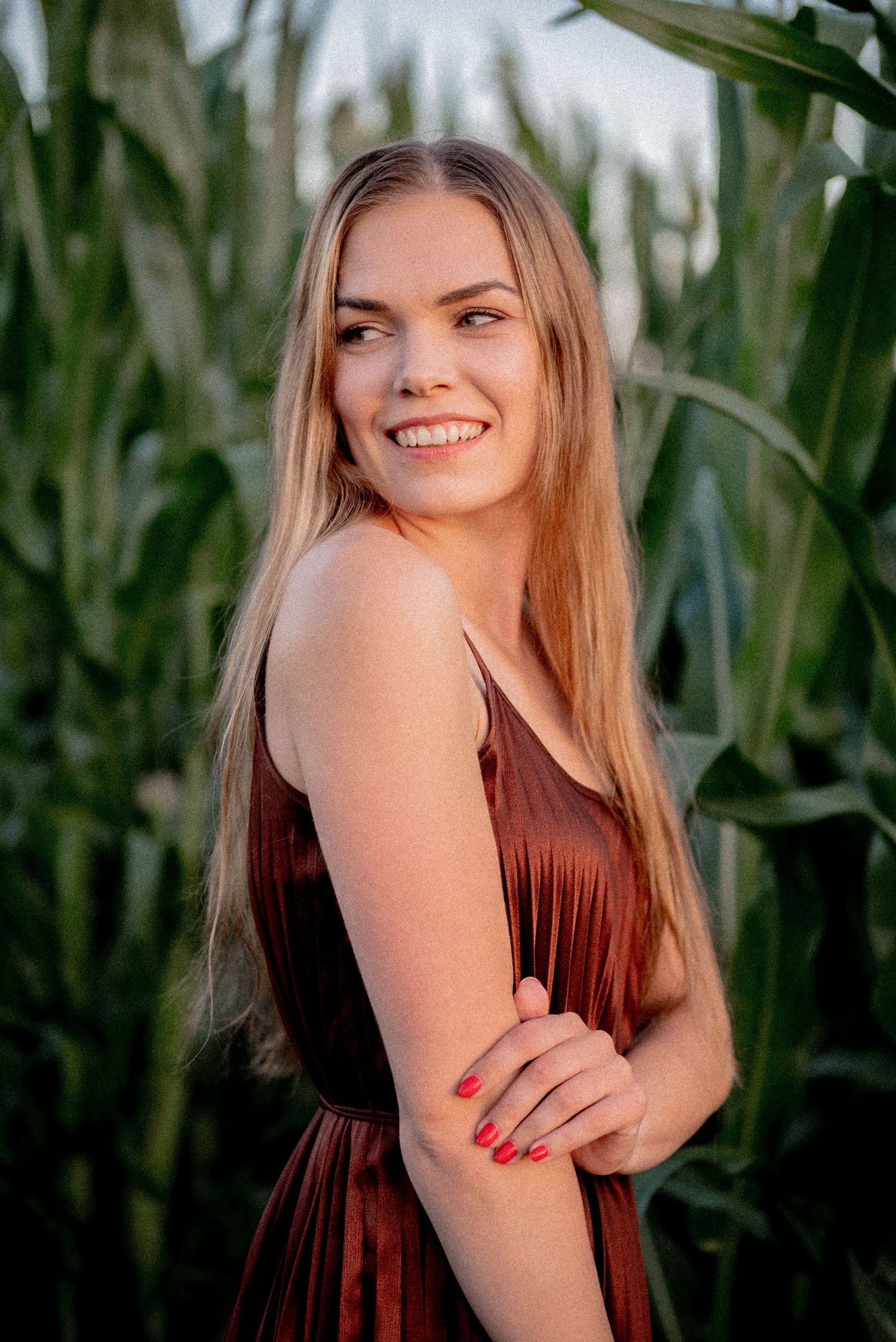 Joyful outdoor portrait in burgundy dress with corn stalks in background.