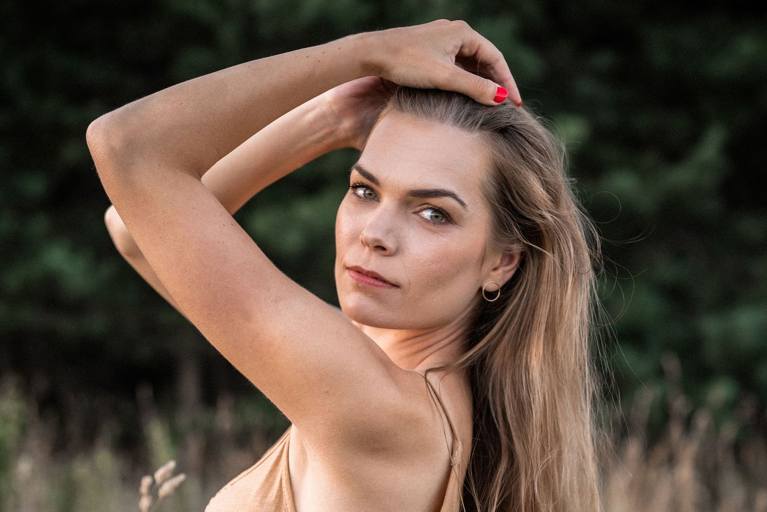 A portrait of a person with long blonde hair posing outdoors with hand in hair.