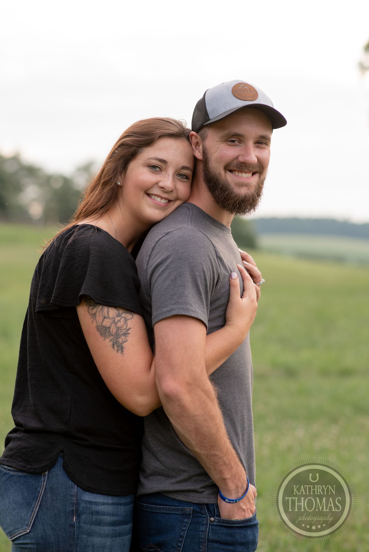 A couple in casual attire embracing outdoors with one wearing a baseball cap.