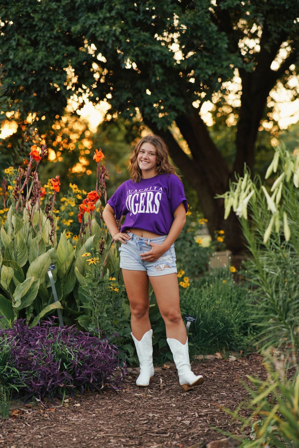 Senior portrait in lush garden with flowers and greenery in soft natural light