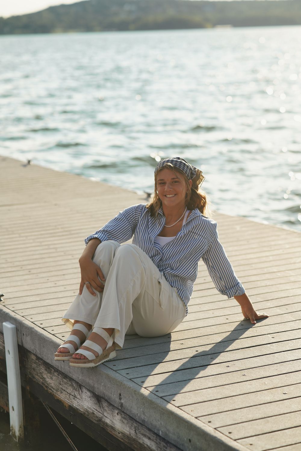 Senior portrait of girl sitting on dock by calm lake with natural lighting