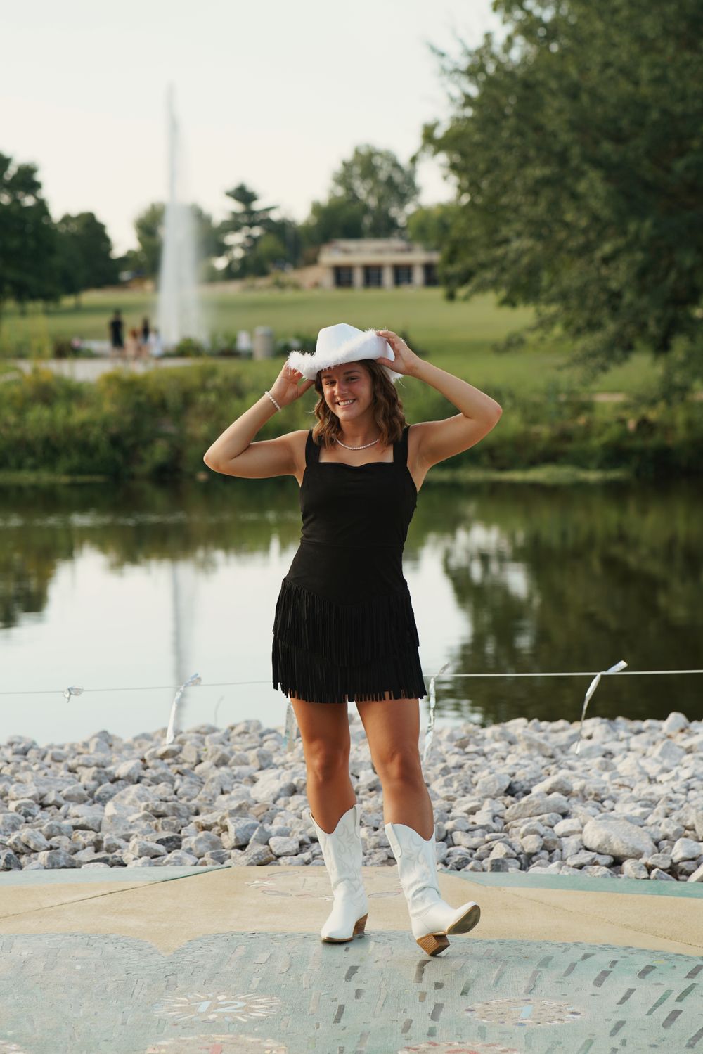Senior portrait in lush garden with flowers and greenery in soft natural light. Lake in background.