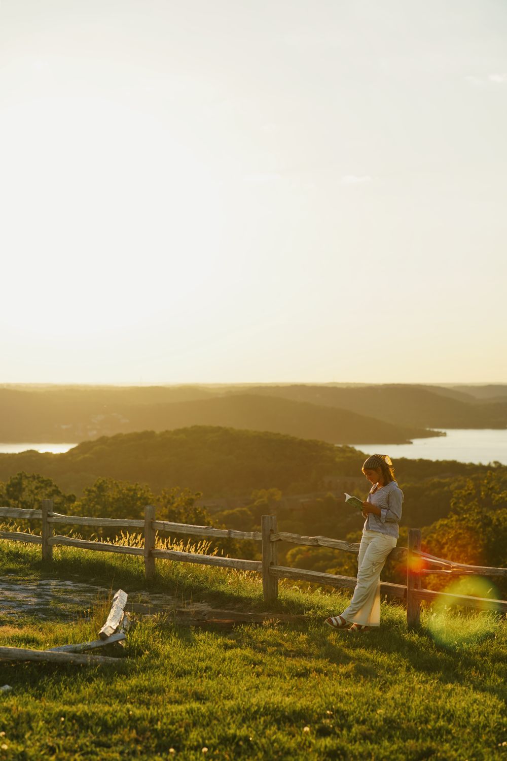 Senior portrait at sunset by lake, surrounded by golden light, reading a book