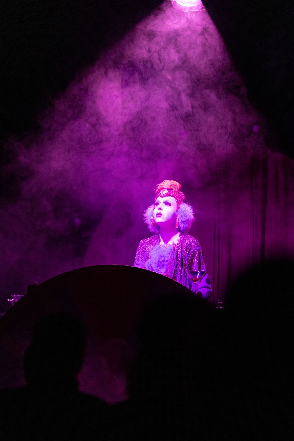 Theatrical performance scene bathed in purple smoke and dramatic spotlight from above.