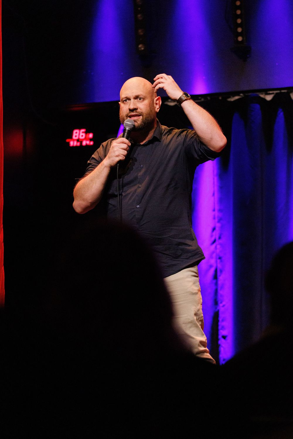 Stand-up comedy performance on stage with purple and red theatrical lighting.