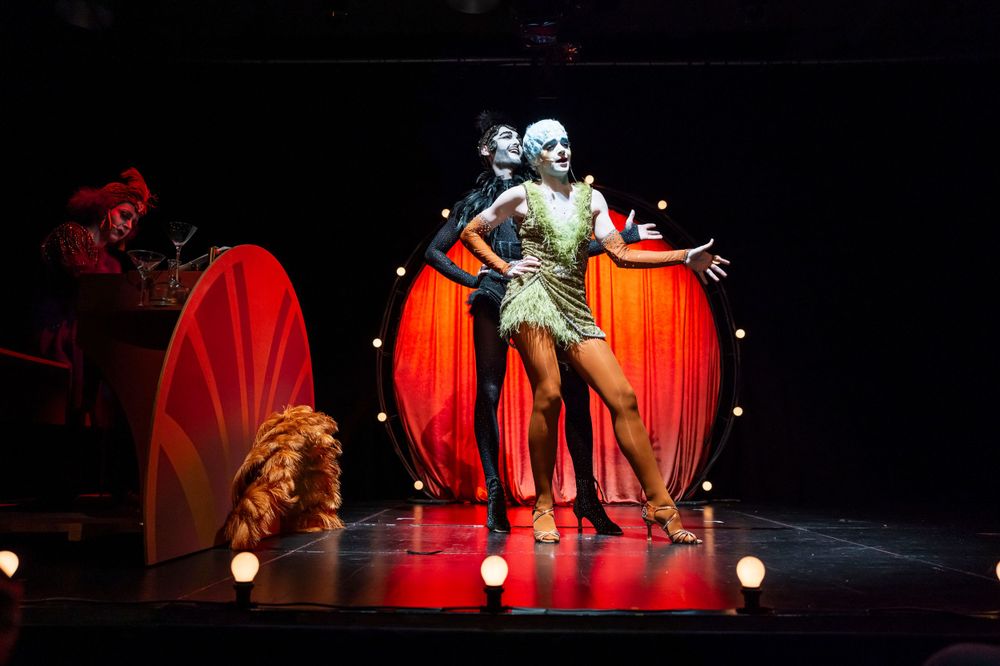 Theatrical performance with dramatic red lighting and decorative set pieces on dark stage.