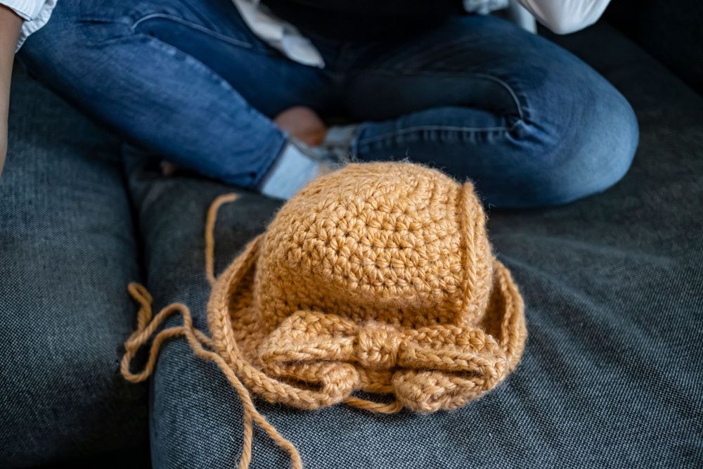Tan crochet project in progress on dark grey couch with yarn.