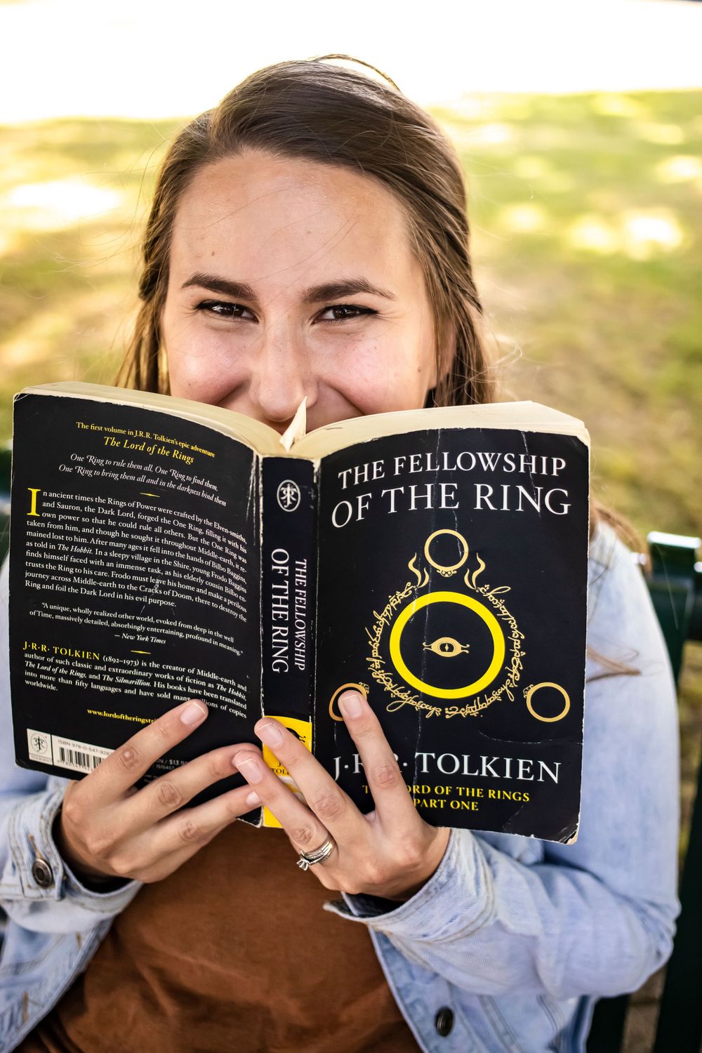 Reader holding The Fellowship of the Ring book outdoors on sunny day.