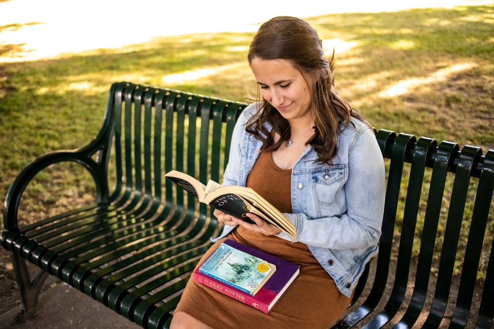 Reading on green park bench in denim jacket on sunny day.