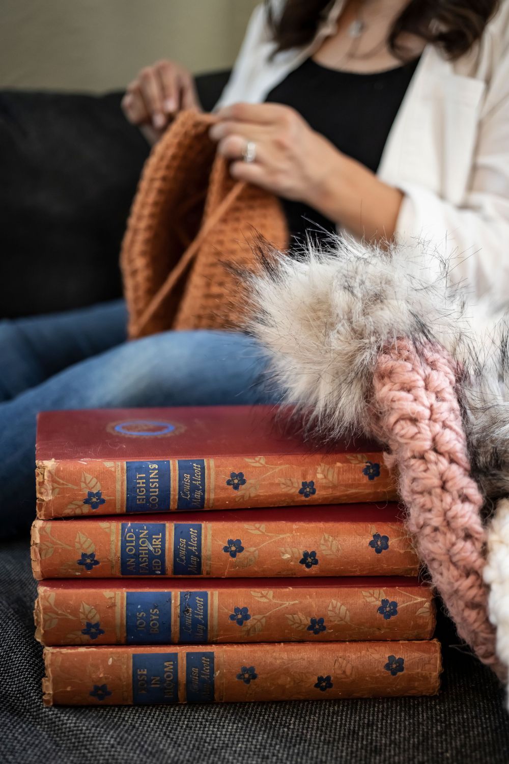 Crocheting hands with vintage books and cozy blanket on dark couch.