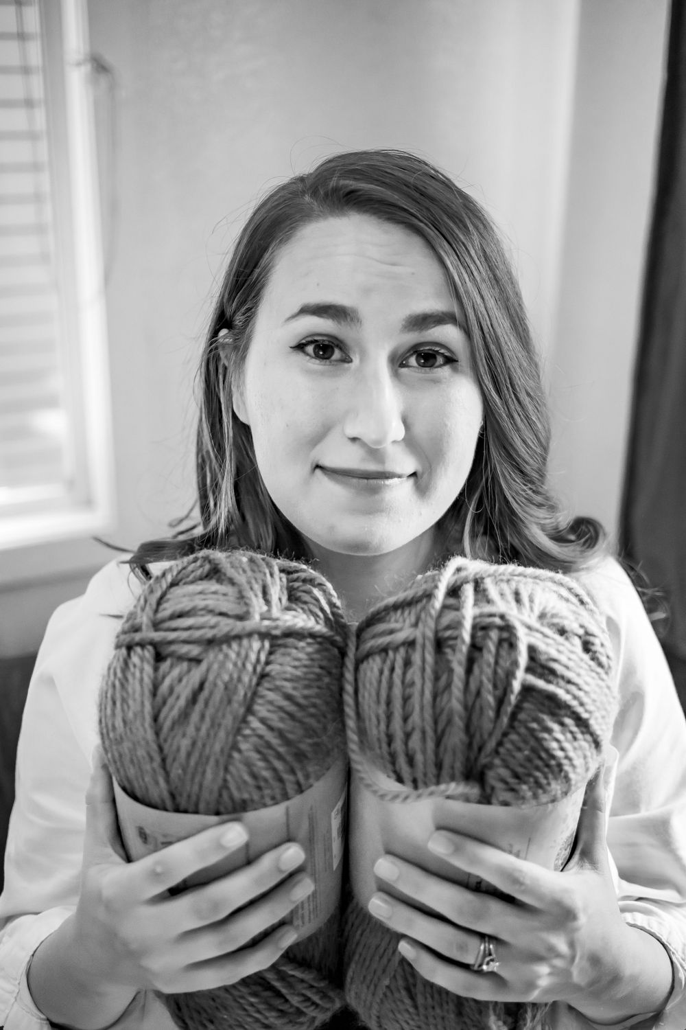 Person holding two large skeins of grey yarn while wearing white sweater.