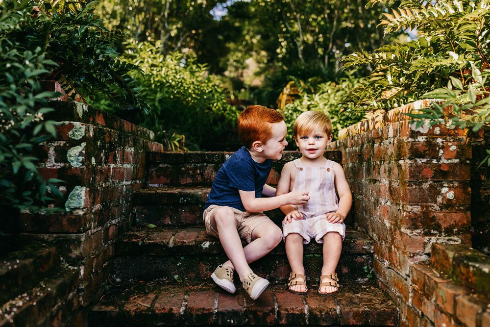 Two children sitting together on brick steps in a lush garden setting.