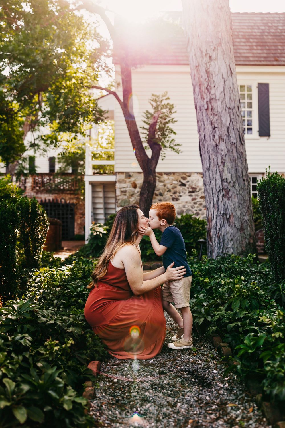 A heartwarming moment shared in a sunlit garden path beside a stone and white house.