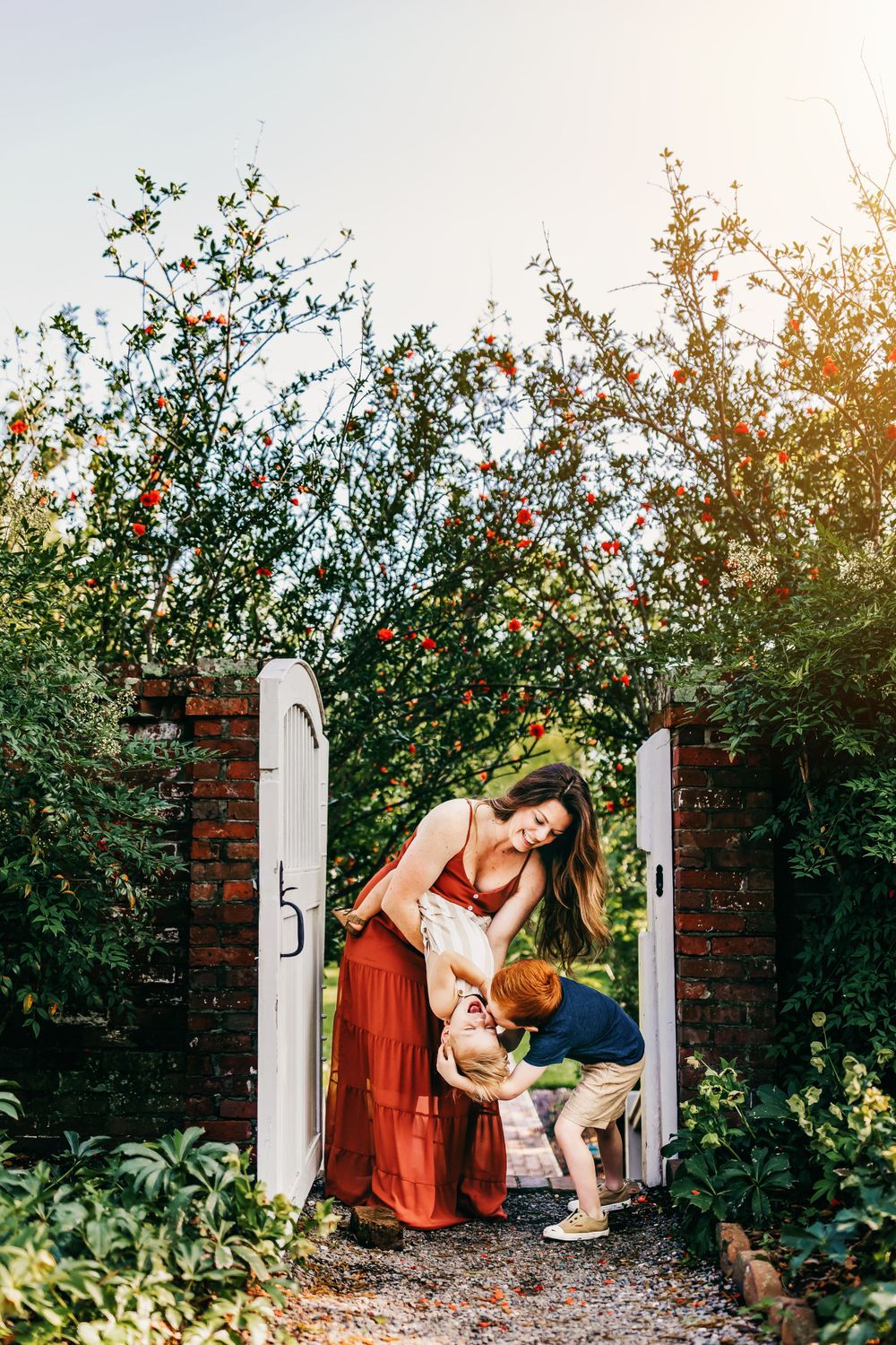 Family moment captured at garden gate with flowering trees and brick pathway.