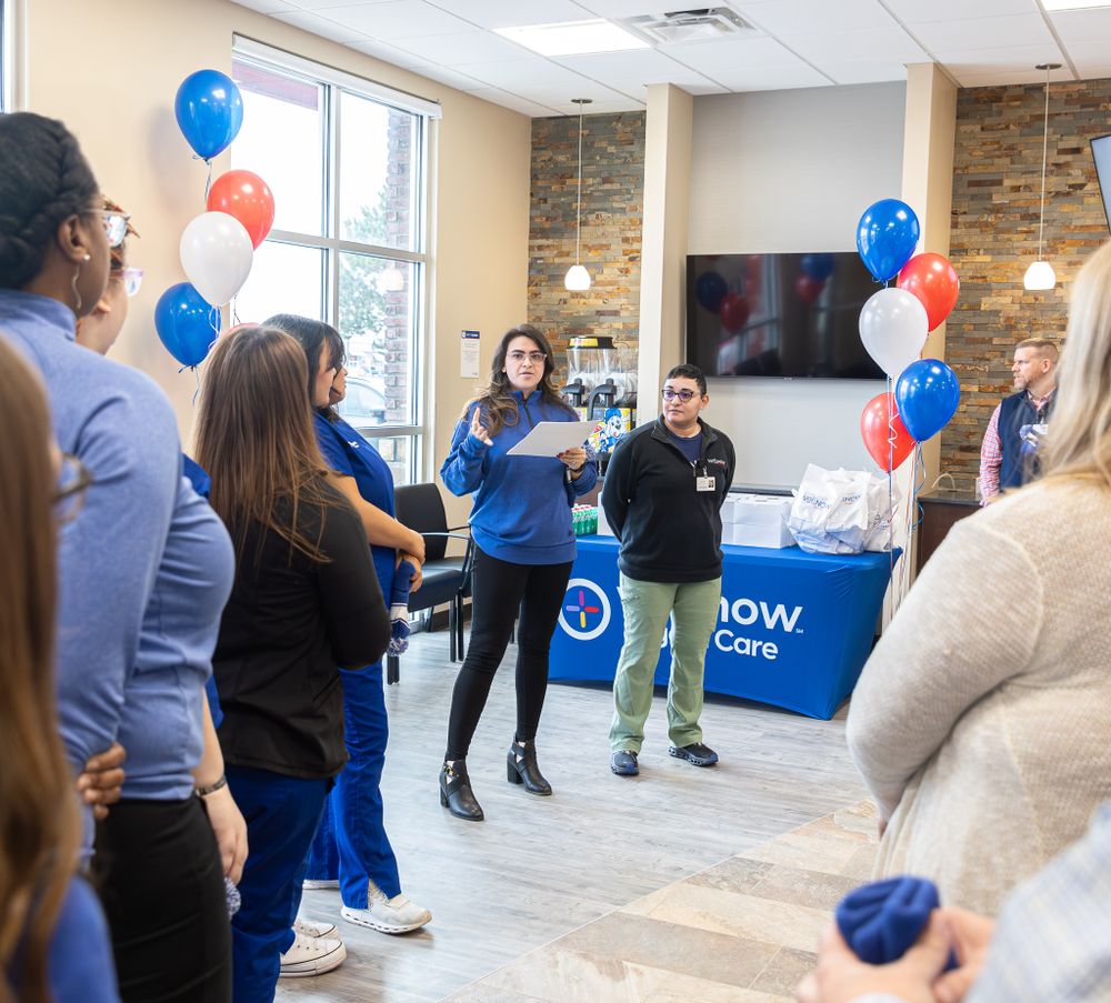 A business meeting with staff gathered around blue and white branded displays and balloons.