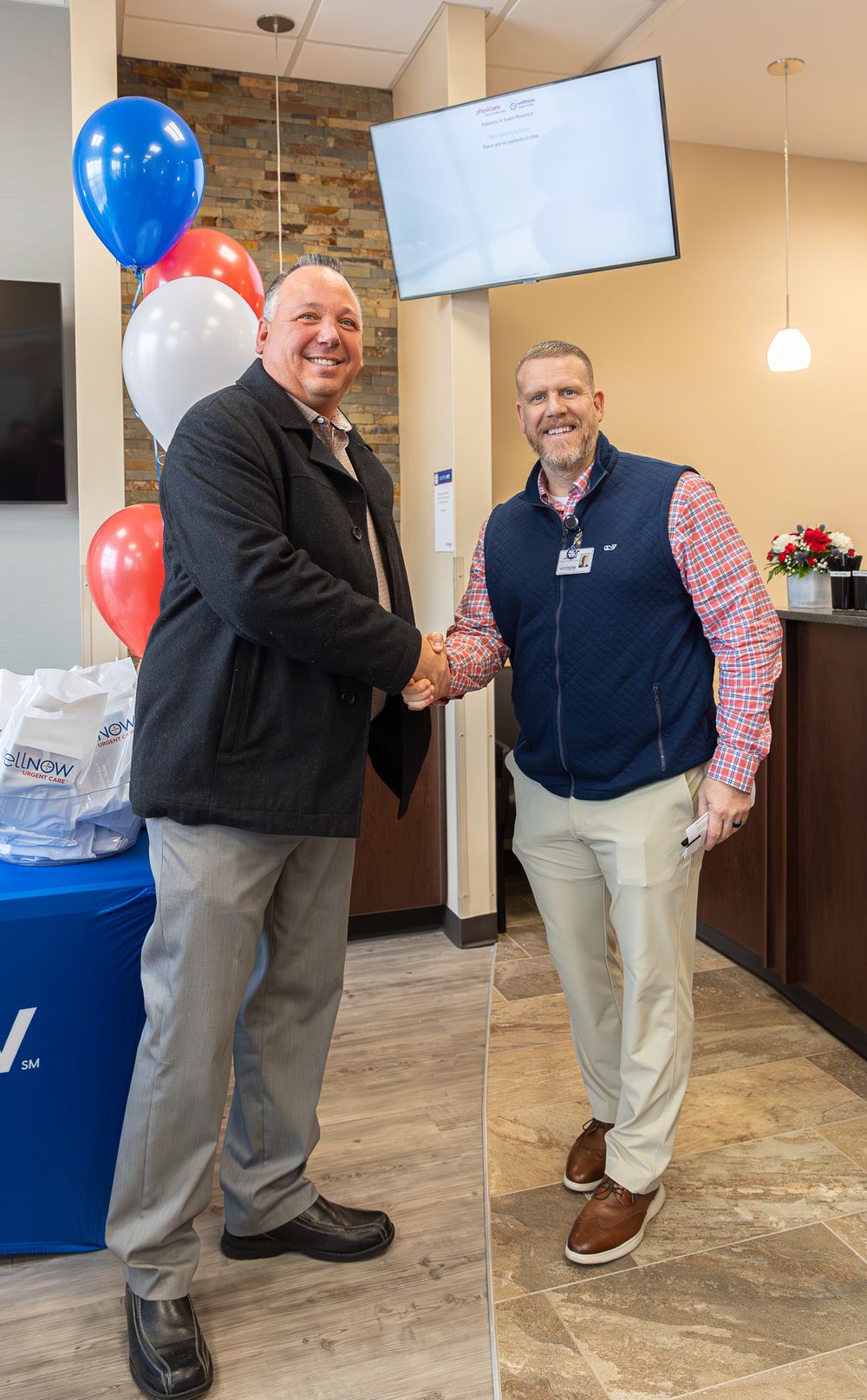 Celebratory handshake between two professionals in an office lobby with patriotic balloon decorations.