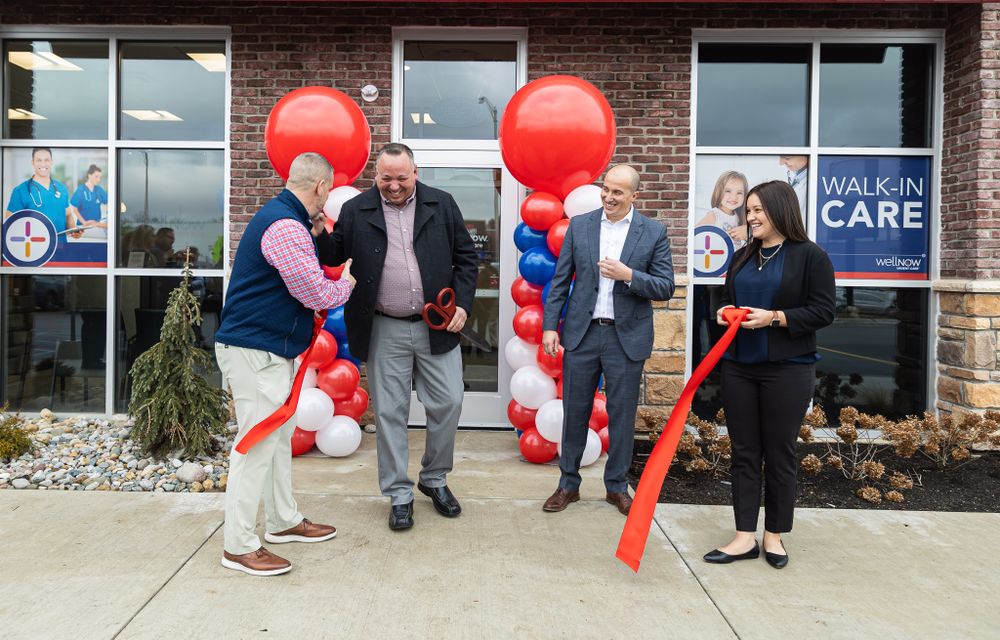 Healthcare facility ribbon cutting ceremony with red and white balloon decorations outside brick building.