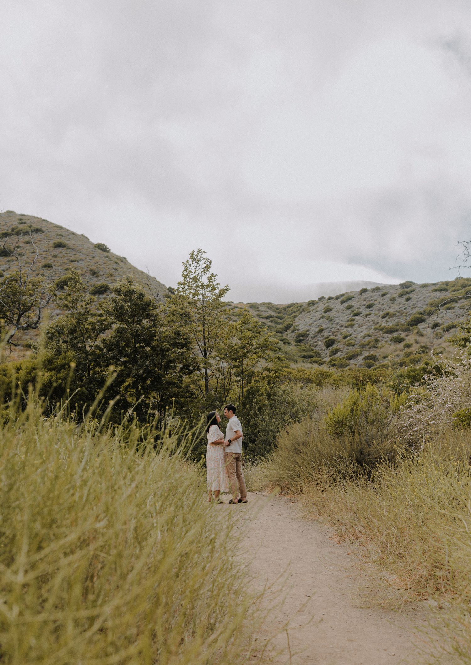 couple looking at each other intimately in front of a mountain covered in greenery