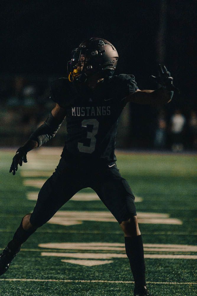 Mustangs football player number 3 in black uniform celebrates on field during night game.