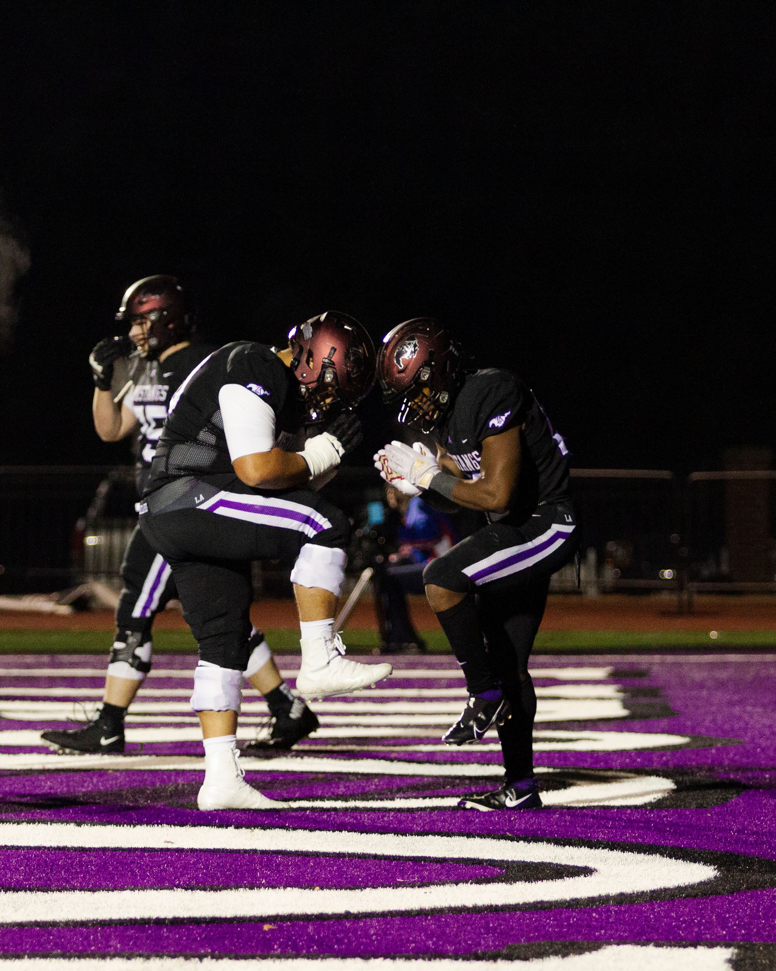 Two football players in black uniforms celebrate together in end zone during night game.