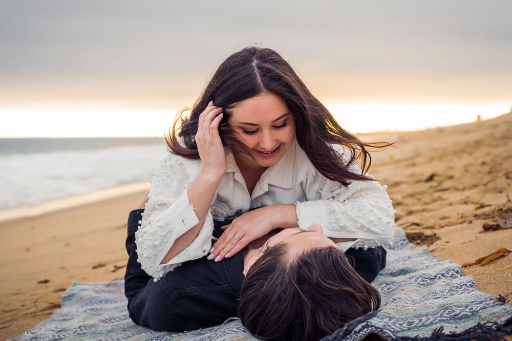 Engaged couple smiles together at the Balboa Fun Zone in Balboa, California. Captured by Chris Cornish Photography.