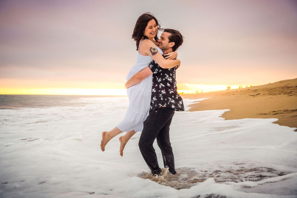 Engaged couple smiles together at the Balboa Fun Zone in Balboa, California. Captured by Chris Cornish Photography.