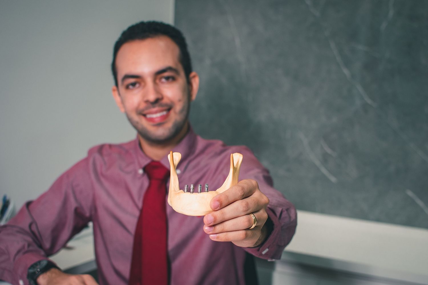Dental professional in burgundy shirt and tie examining jaw model.