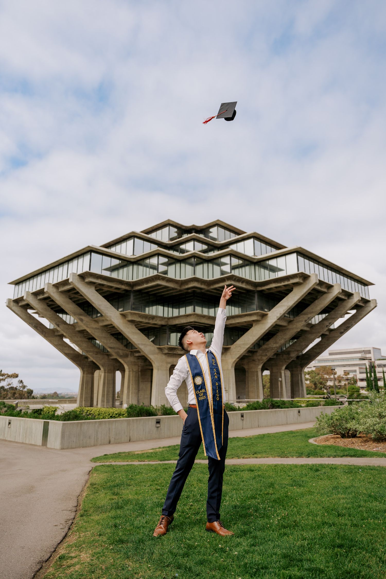 Graduate celebrating near the iconic Geisel Library building at UC San Diego throws cap in the air.