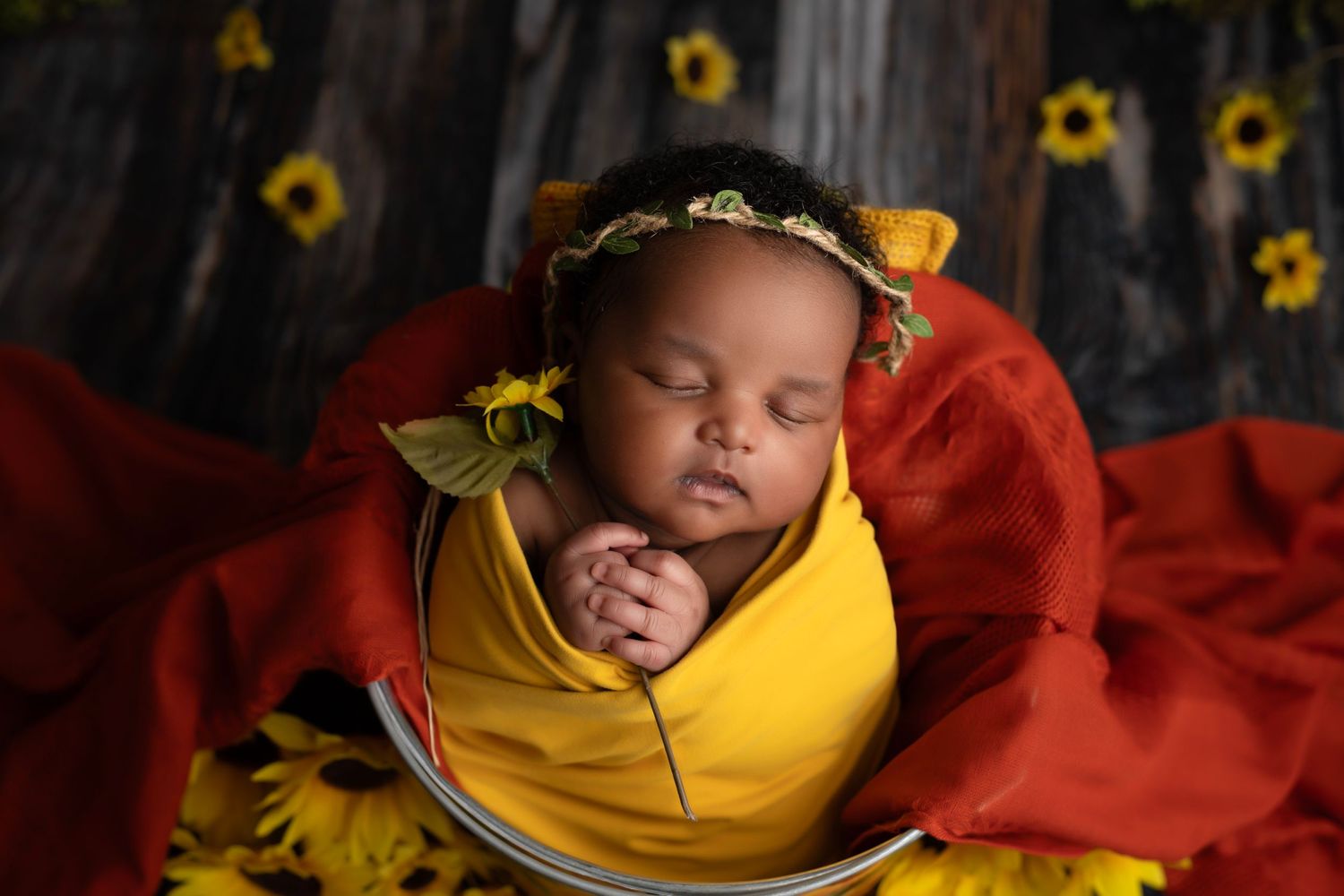 Creative newborn portrait surrounded by bright sunflowers and yellow wrapping.