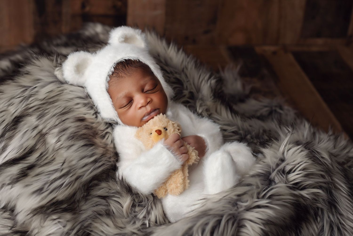 Newborn photography session featuring soft grey fur blanket and peaceful sleeping pose.