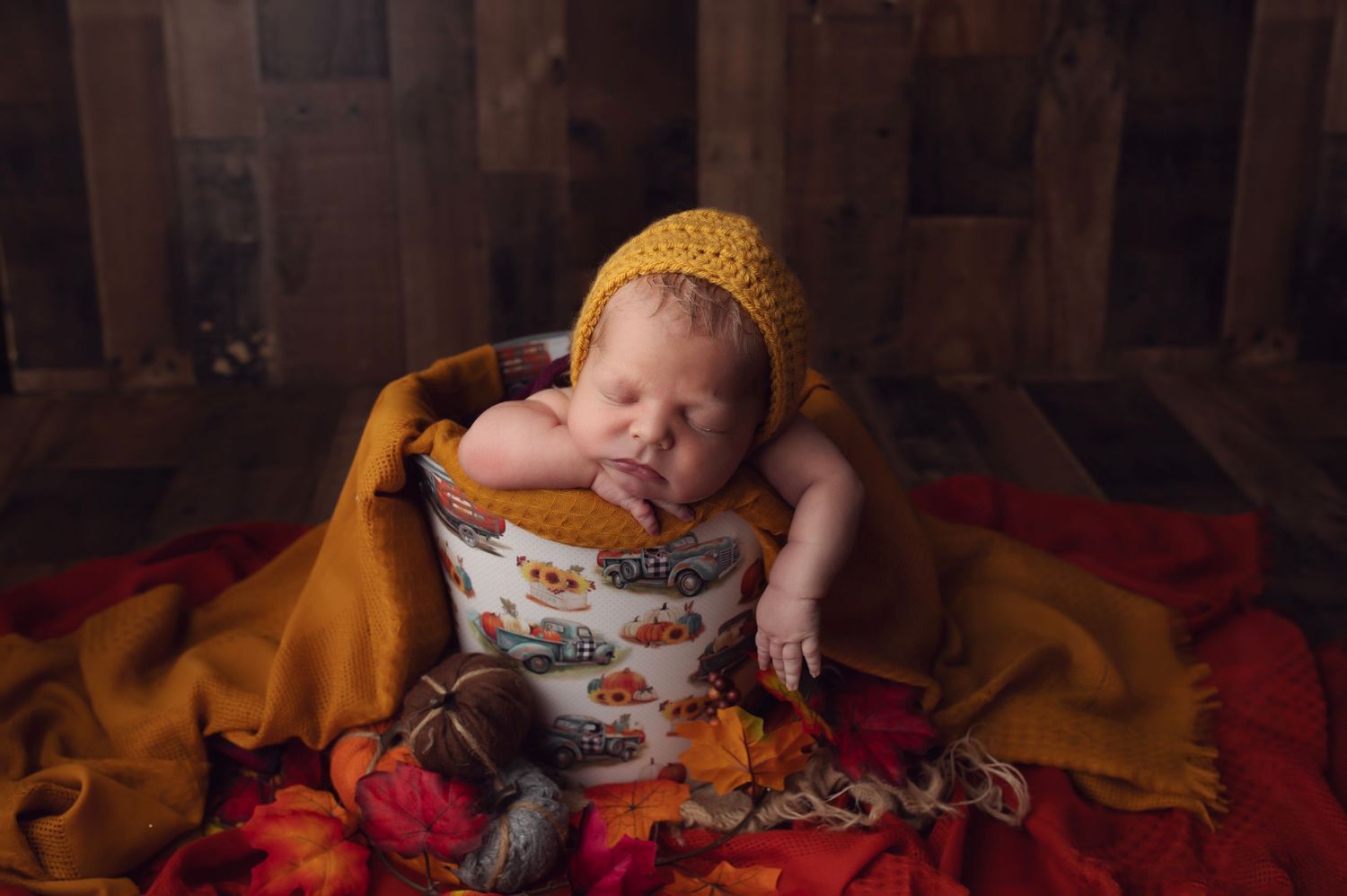 Sleeping newborn wearing yellow hat on orange blanket in rustic setting.