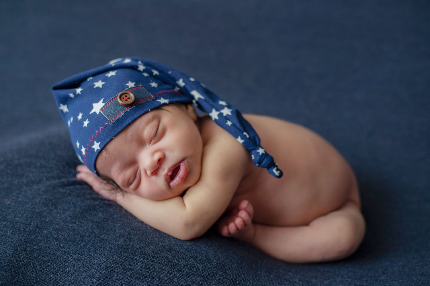 Peaceful newborn baby sleeping on moon-shaped pillow with starry backdrop.