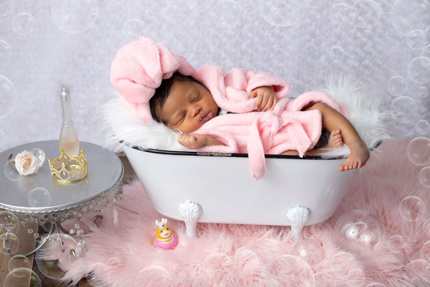 A sleeping baby in pink outfit posed in vintage white bathtub with pink decor.