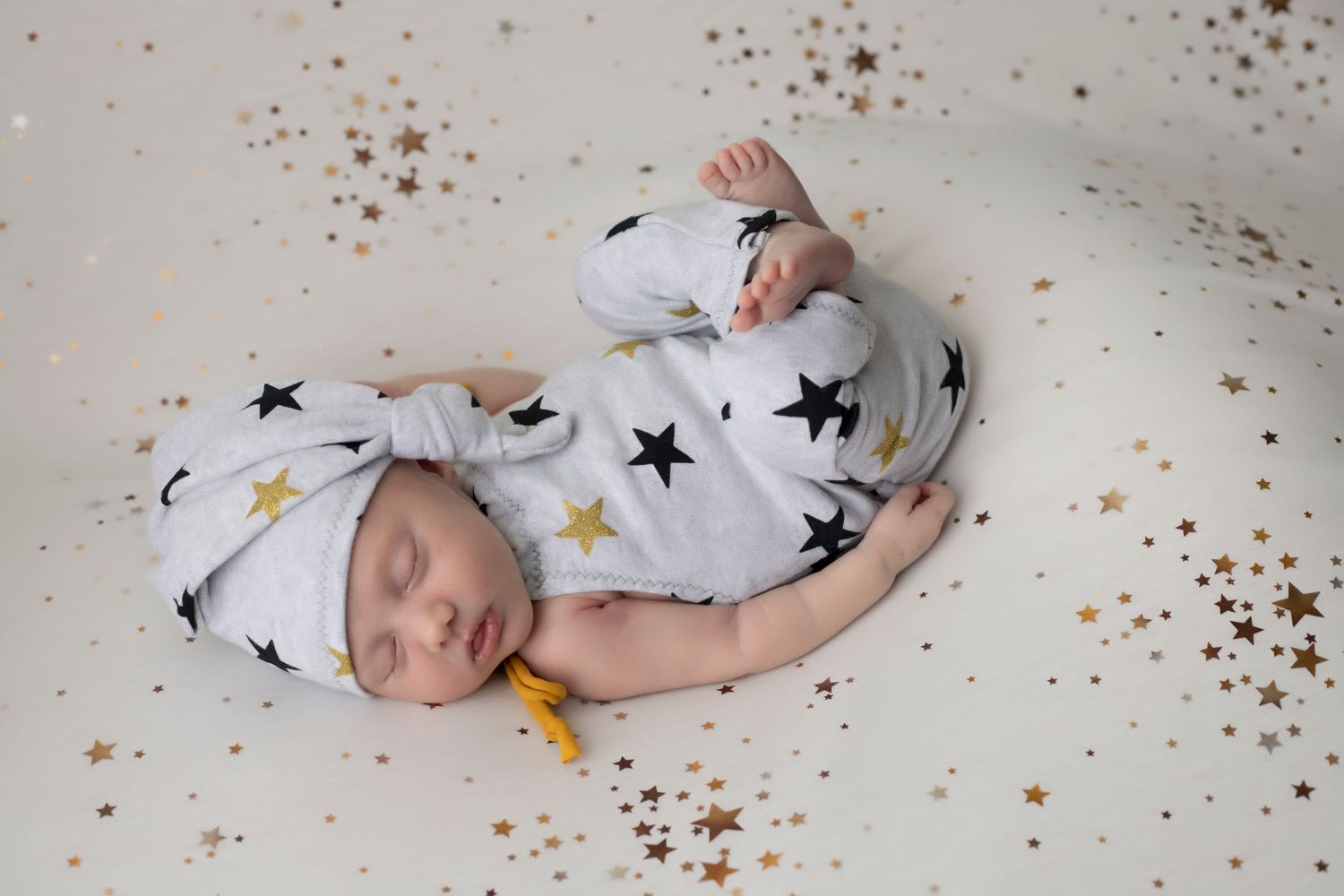 Minimalist newborn photo with star pattern fabric and gold sparkle accents.