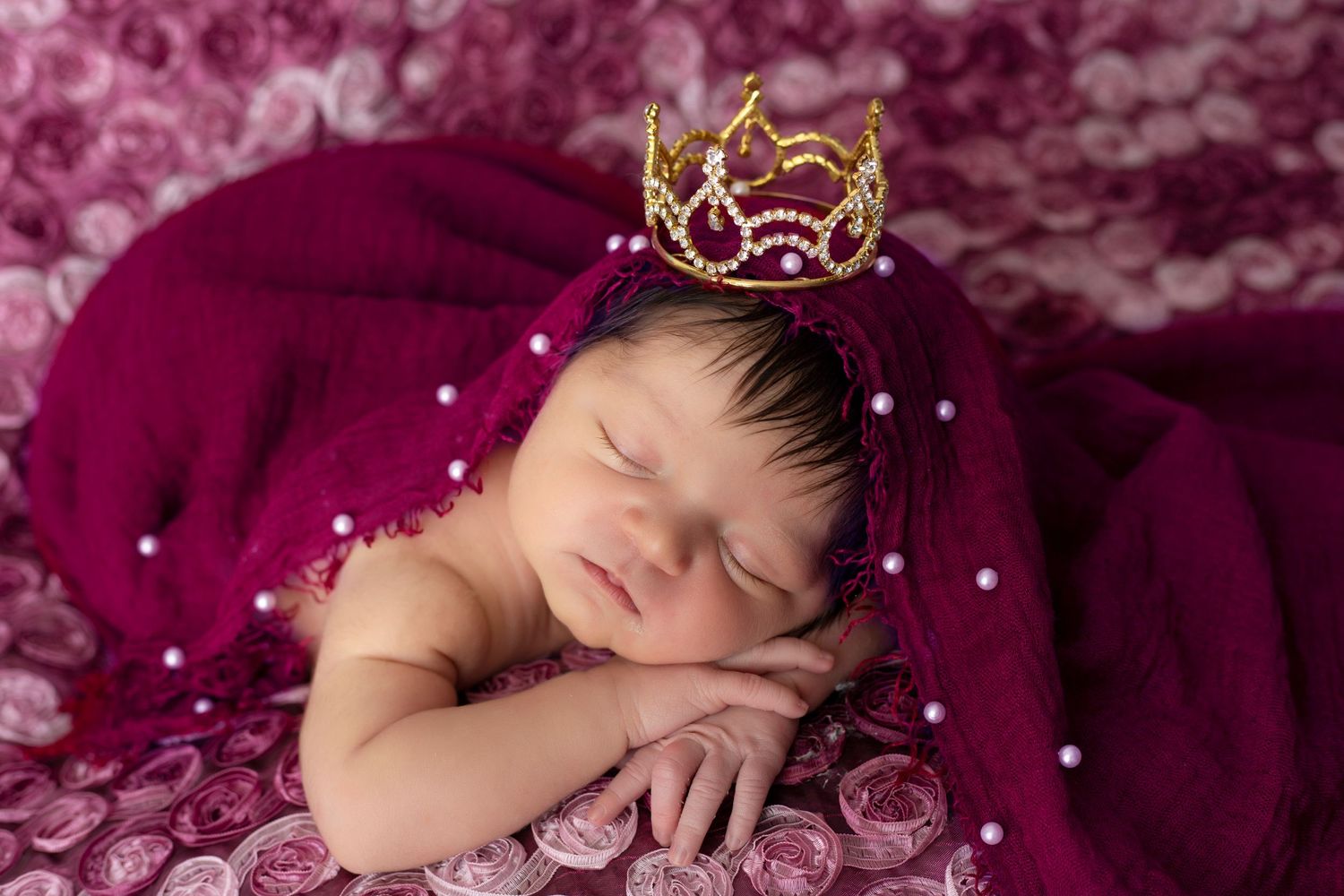 Elegant newborn photo session with burgundy fabric and sparkling crown accent.