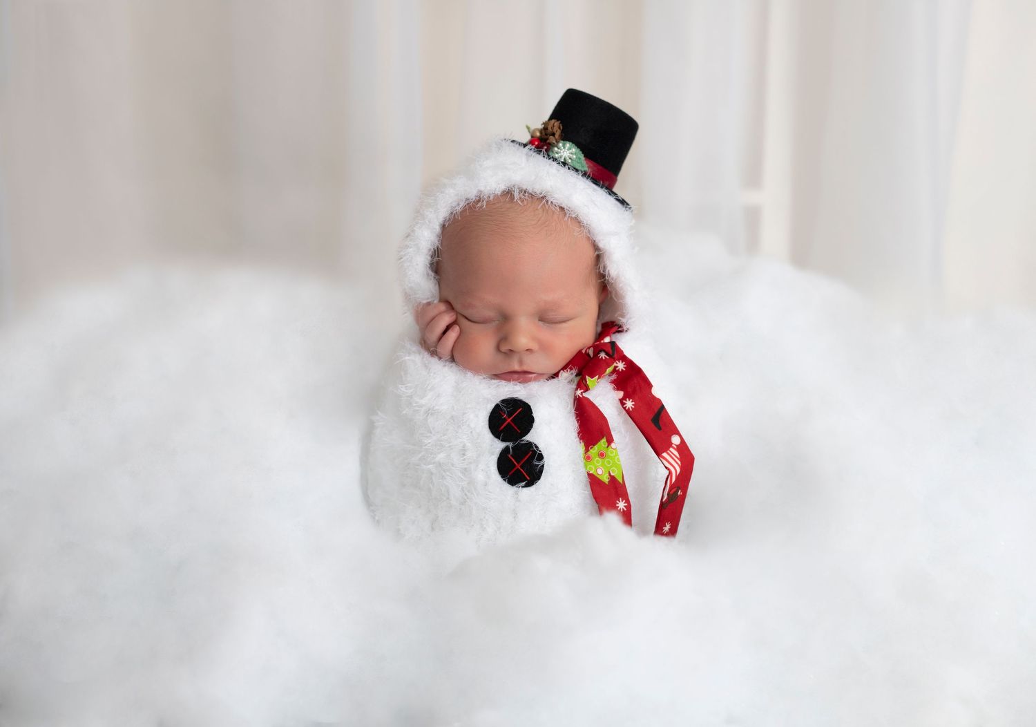 A winter-themed newborn photo with snowman accessories on white fluffy background.