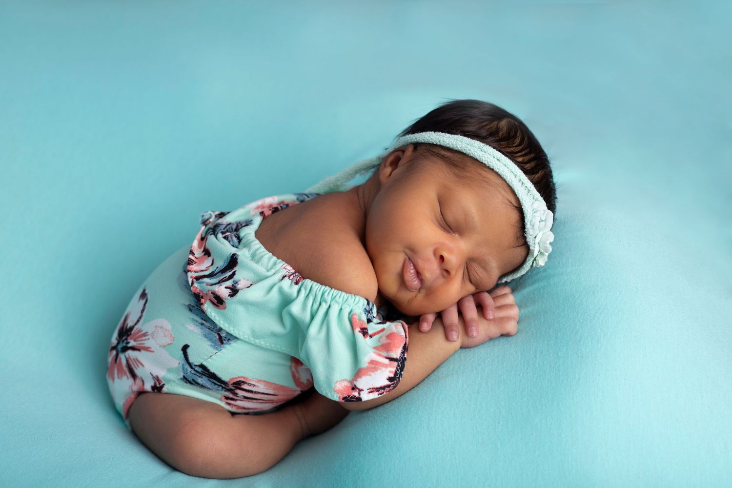 A sleeping baby in turquoise floral outfit against blue background.