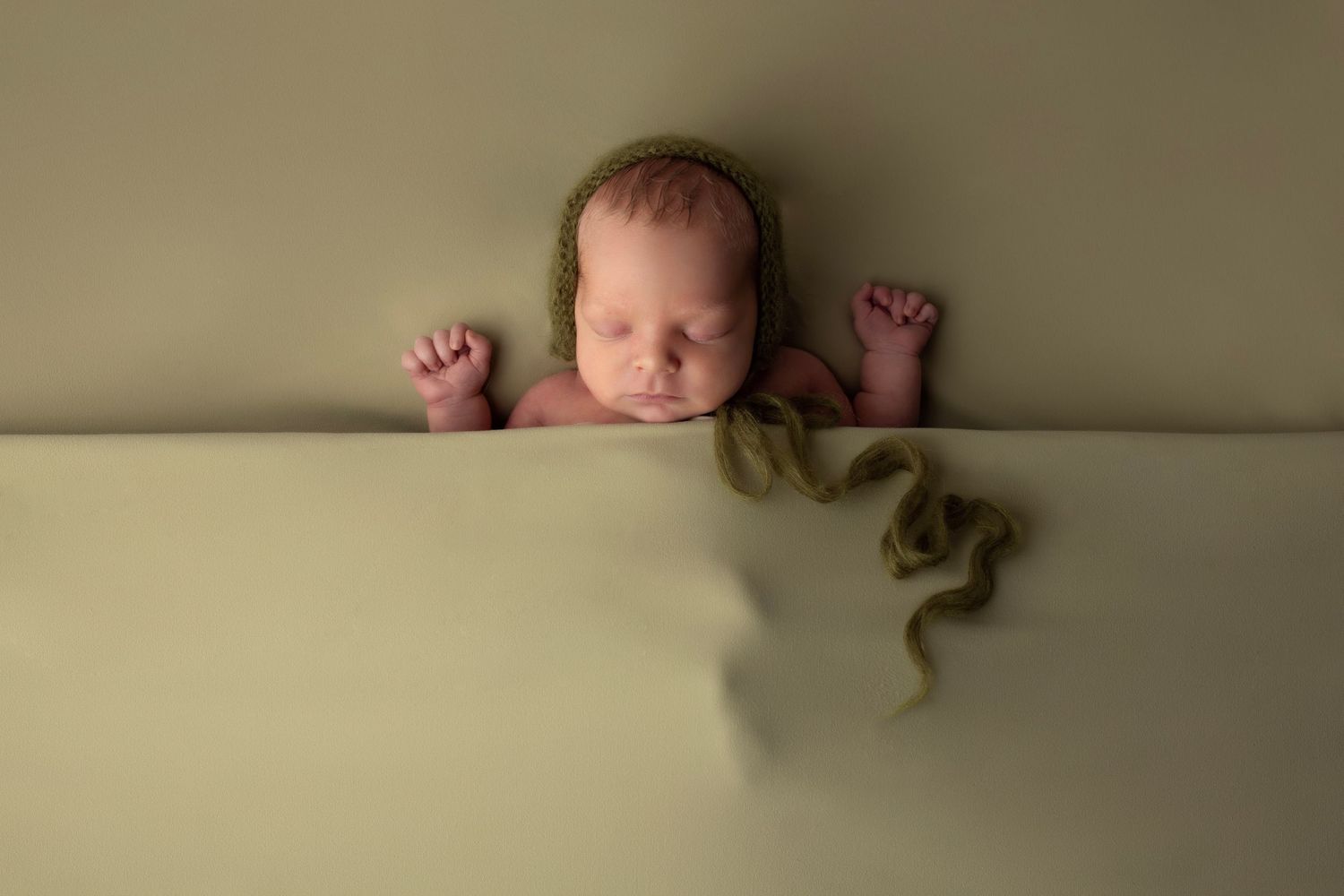Simple newborn portrait with baby peeking over neutral backdrop.