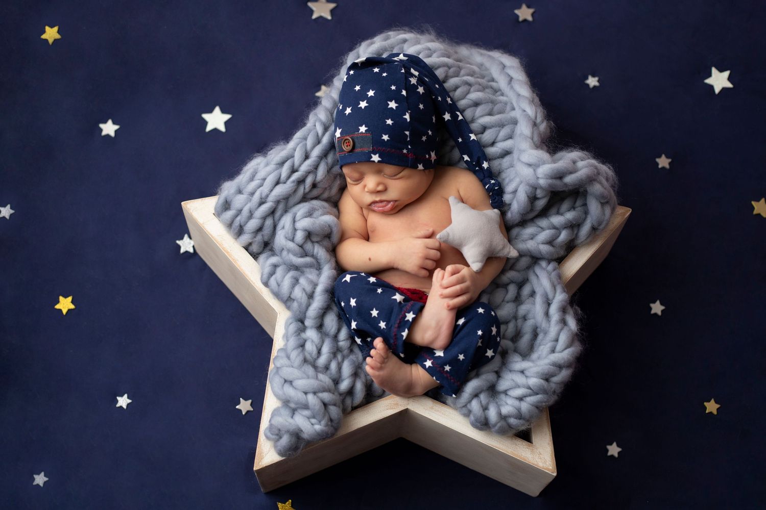 Artistic newborn photo with baby sleeping on star prop against night sky backdrop.