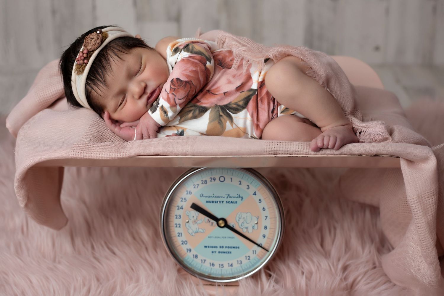 Artistic newborn portrait with vintage clock prop and soft pink backdrop.