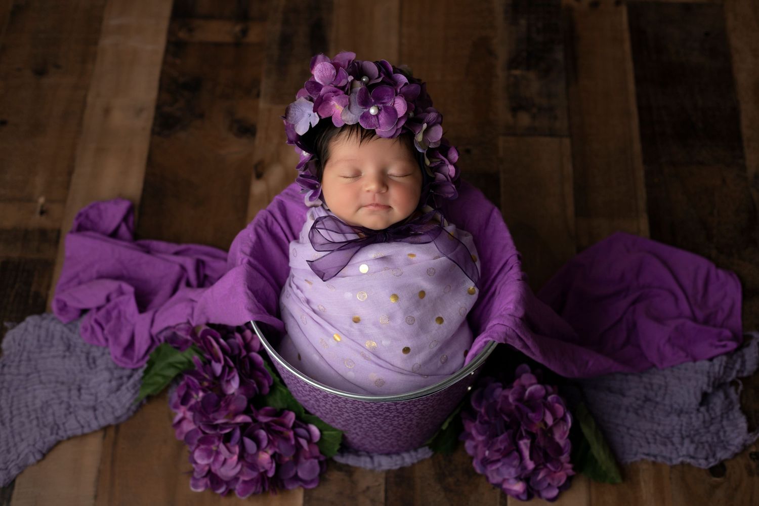 Dreamy newborn portrait with purple flowers and soft lavender wrapping.