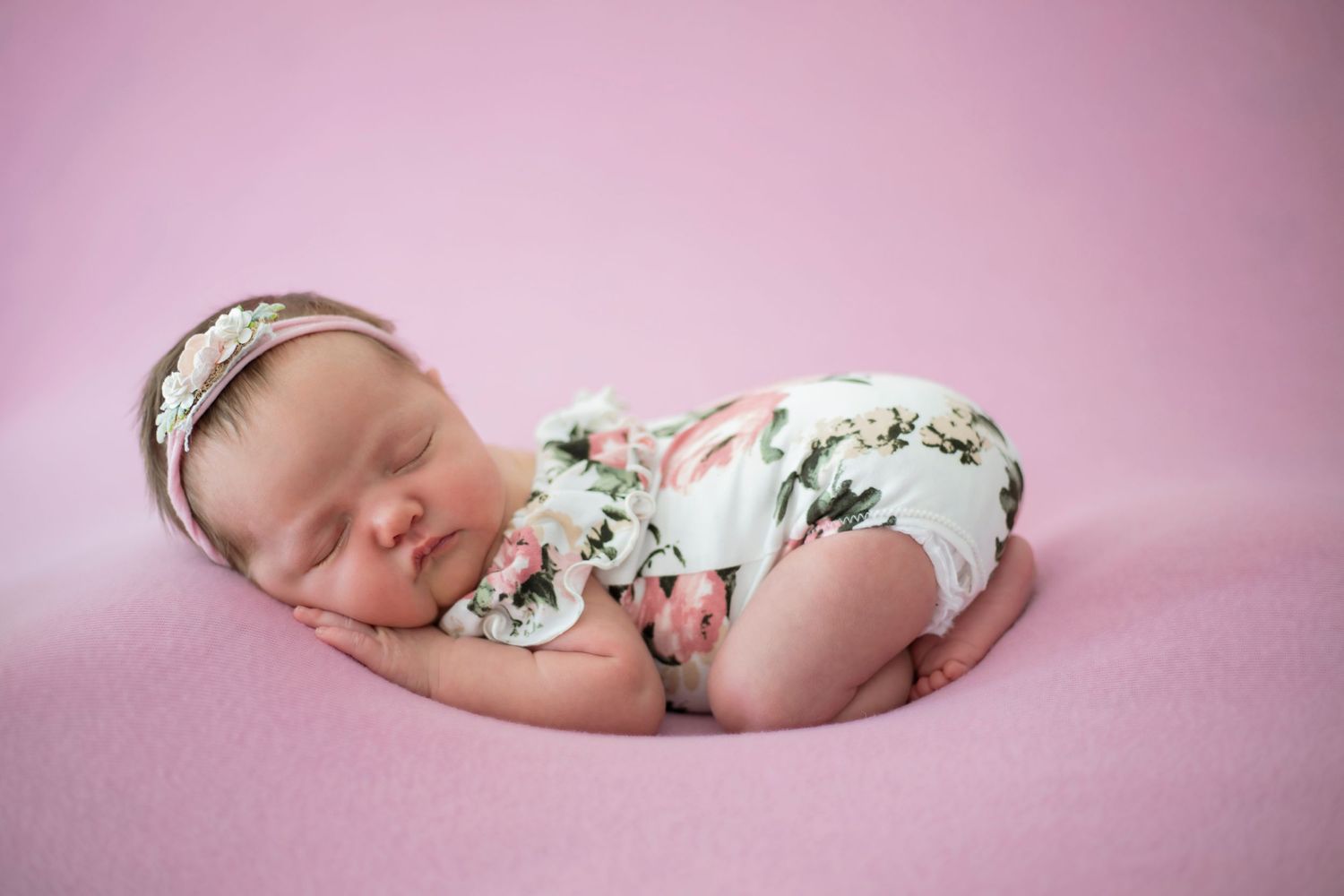 Sleeping newborn in floral outfit against pink studio background.