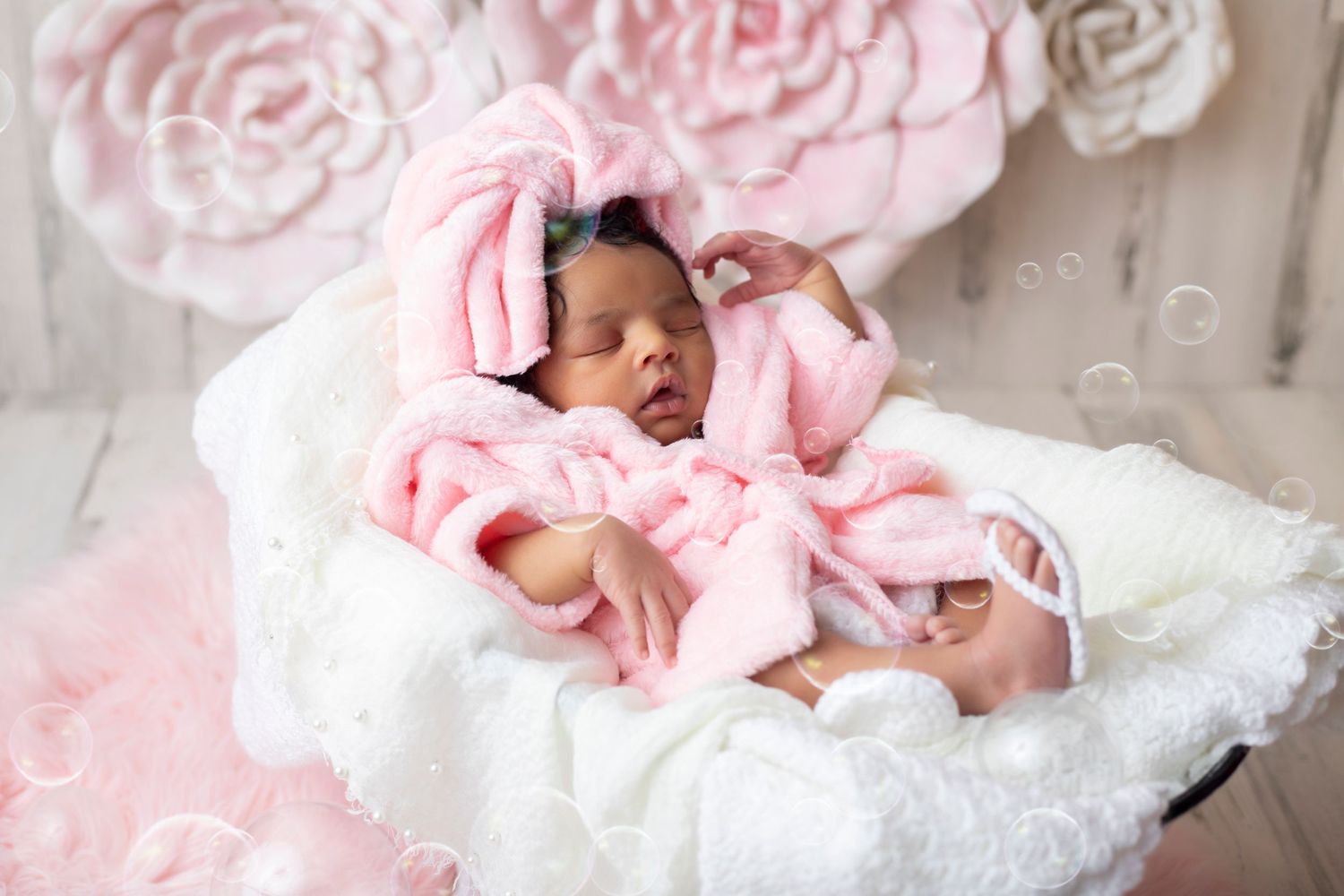 Newborn baby sleeping on soft pink blankets in a dreamy studio setting.