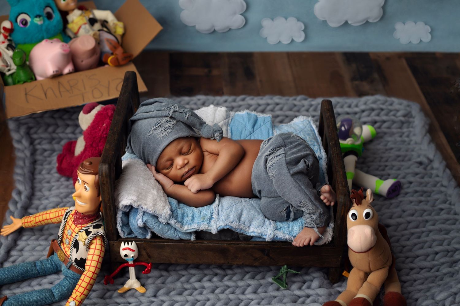 Newborn sleeping on tiny bed surrounded by Toy Story characters and plush toys.